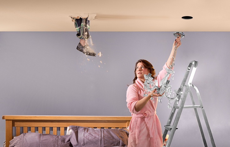 A husband's foot comes through the bad floor of his attic as his wife is hanging a chandelier in their bedroom.