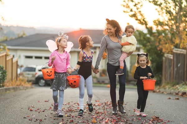 adult trick or treating with group of young children before dusk