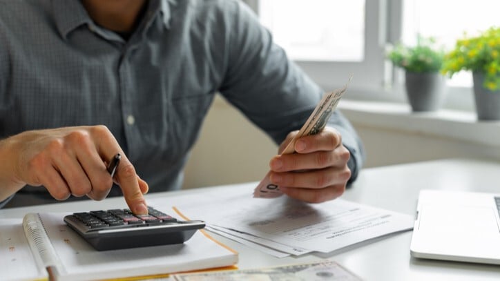 man holding cash and using a calculator