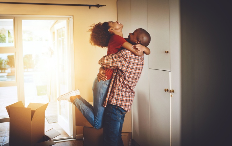 A happy couple is embracing with the holding his partner in the air with joy. They are celebrating the purchase of their new house.