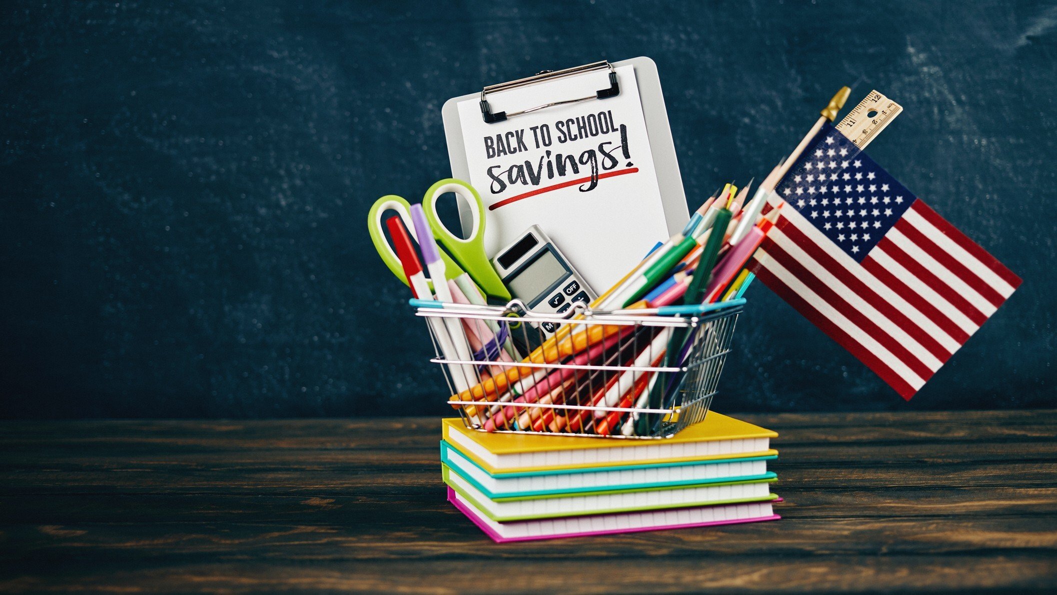 Back to School Savings. basket of school supplies, an american flag, sitting on a pile of notebookes.