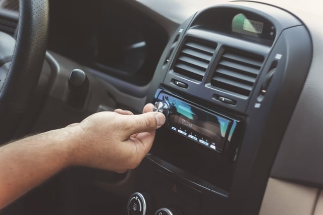 man hand turning up volume on car radio