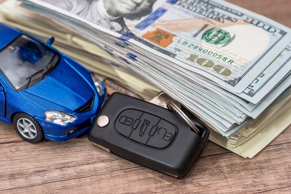 money and car keys stacked next to blue car