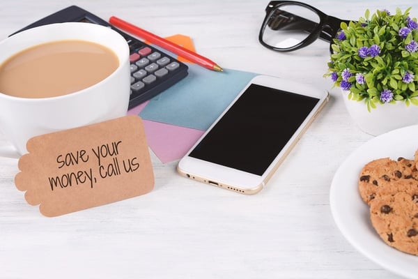 paper note with text 'save your money, call us' with coffee, cookies and calculator on white wooden background