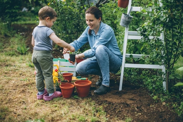 toddler and mother watering potted plants in garden