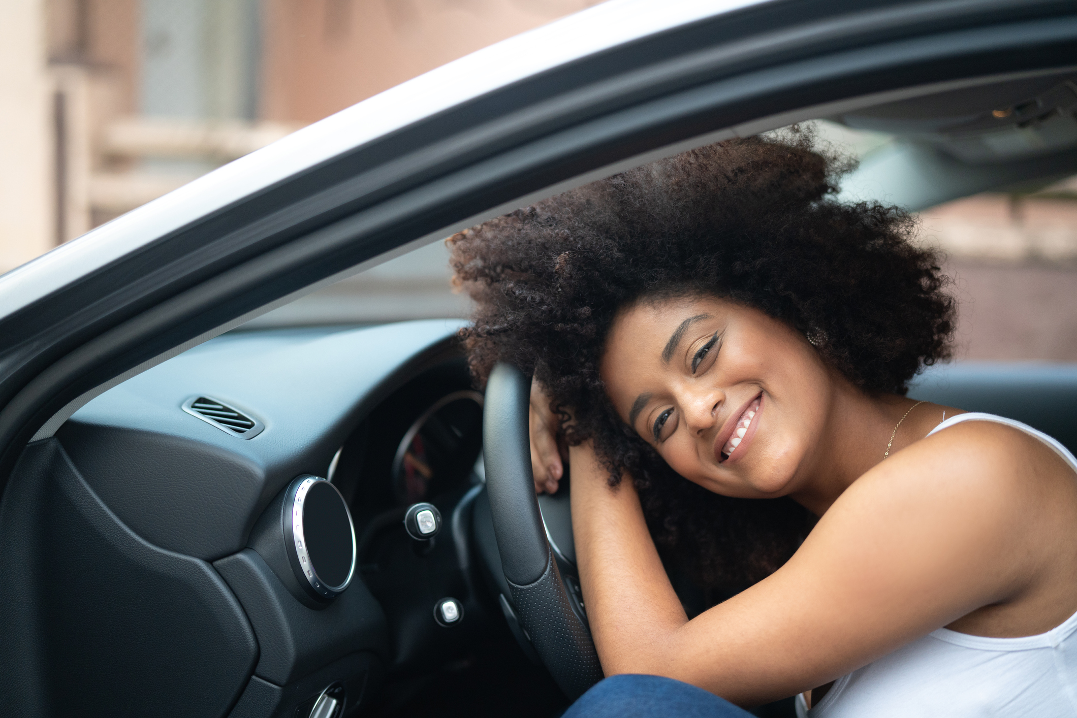 Young woman happily hugging the steering wheel of a car